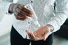 A person squeezing a plastic bottle of hand sanitizer into their palm