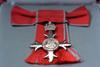 Close up of a cross-shaped MBE medal with a red ribbon