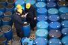 A photo of men in hard hats and overalls checking barrels of chemicals