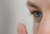 A close-up photo of a man putting a contact lens into his eye
