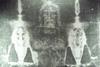 An enhanced black and white image of the Turin Shroud featuring a faint image of a bearded man's face some a damaged cloth