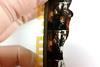 Close up of a damaged strip of celluloid film held by a hand in latex gloves. The film features two women in mid-century living room and clothing but the film is cracked and broken and parts of the images have turned white.