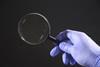 A hand in a latex glove holding a magnifying glass