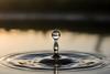 A single water droplet creates ripples on a serene lake surface at sunset
