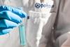 A close up of a person wearing a branded Polypure lab coat holding a test tube of pale blue liquid