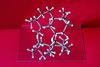 A photo of a molecular model of drimane, a bicyclic natural product, sitting on top of a mirror on a velvet red background