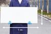 A man in a blue lab coat and latex gloves holding a white board 1 m by 0.5 m