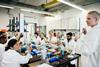 A cluttered lab bench full of apparatus slightly obscures the students working at it, as they perform an experiment as part of their training