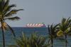 A tanker ship on the Strait of Hormuz in the ocean as seen from the shore where there are palm trees