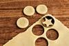 Rolled out raw cookie dough with three round cookies and their corresponding holes. There is a fourth round hole being cut out but the cookie cutter but the cookie is star-shaped.