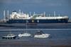 A large LNG tanker ship in an industrial port. In the foreground are small pleasure boats.