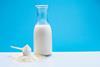 An image of powdered milk, in a scoop, next to a pitcher of liquid milk.