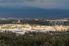 An aerial view of Los Alamos National Laboratory in the USA. There a number of low-rise office-type buildings surrounded by forest with cloud-topped mountains in the distance
