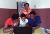 A photo of a woman and three children gathered around a laptop