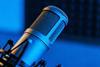 A detailed close-up of a silver microphone on a stand, positioned in a recording studio with a blue-lit background, showcasing its metal mesh grill and cylindrical body