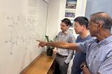 Three men discussing chemical structures drawn on a whiteboard