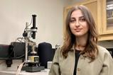 A photograph of Alaa Al-Shaer standing in front of a microscope