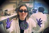 A woman in a laboratory wearing sunglasses, latex gloves and a white coat rapping about DNA