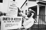 A black and white image of a policeman in Seveso, Italy pinning up warning signs written in Italian warning of chemical contamination of the area