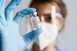 A photograph of a researcher wearing eye-protection, gloves and a mask, holding a vial containing an mRNA vaccine