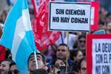 A large group of protesters. One is holding an Argentinian flag without the sun and one is holding a placard that says Sin Ciencia No Hay Conan (Without Science we have no Conan)