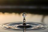 A single water droplet creates ripples on a serene lake surface at sunset
