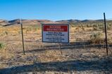 A landscape of dry mountainous grassland with clear blue sky. A sign in on a barb wire fence in the foreground says: Access Restricted/ Active Mine Site/Thacker Pass Project/ For access please call Lithium Nevada Corp