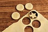 Rolled out raw cookie dough with three round cookies and their corresponding holes. There is a fourth round hole being cut out but the cookie cutter but the cookie is star-shaped.