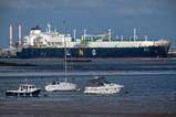 A large LNG tanker ship in an industrial port. In the foreground are small pleasure boats.