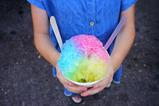Child's hands holding a paper cup filled with rainbow slushee, high angle