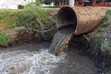 A sewage pipe empyting into a river near some buildings