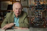 A photograph of James Watson sitting next to a molecular model of DNA's double helix