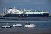 A large LNG tanker ship in an industrial port. In the foreground are small pleasure boats.
