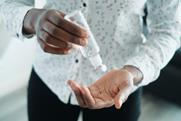 A person squeezing a plastic bottle of hand sanitizer into their palm