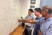 Three men discussing chemical structures drawn on a whiteboard