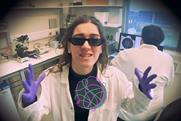 A woman in a laboratory wearing sunglasses, latex gloves and a white coat rapping about DNA