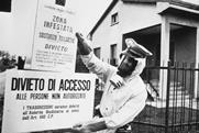 A black and white image of a policeman in Seveso, Italy pinning up warning signs written in Italian warning of chemical contamination of the area