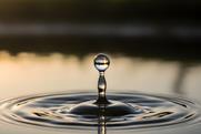 A single water droplet creates ripples on a serene lake surface at sunset
