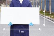 A man in a blue lab coat and latex gloves holding a white board 1 m by 0.5 m