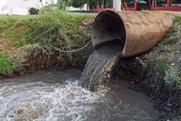 A sewage pipe empyting into a river near some buildings