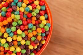 A bowl of small ball fruit-flavored breakfast cereal on a wooden kitchen table