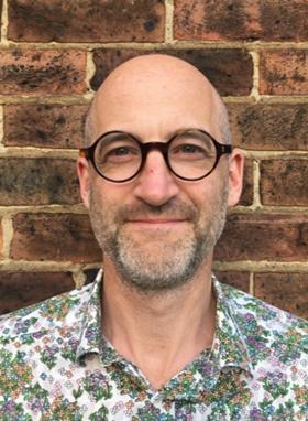 Portrait headshot of Mark Miodownik standing in front of a brick wall
