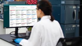 Scientist in lab monitoring multiple instruments using Waters System Monitoring software on a desktop screen