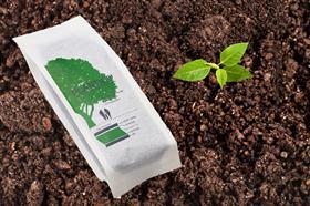 Image shows fresh coffee packaging on soil and a plant beside it