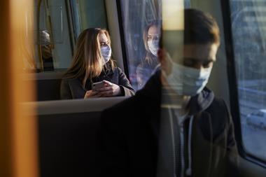 A woman sitting on a train wearing a medical mask
