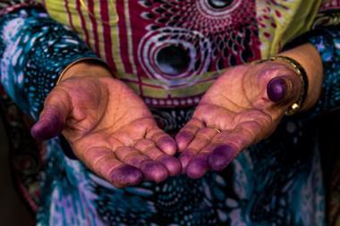 A Bandari woman showing her hands with indigo traces after sewing a traditional burqa mask