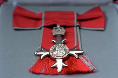 Close up of a cross-shaped MBE medal with a red ribbon