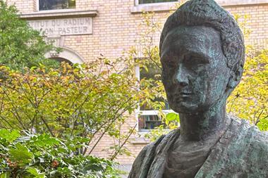 A bronze bust of Marie Curie in a courtyard garden