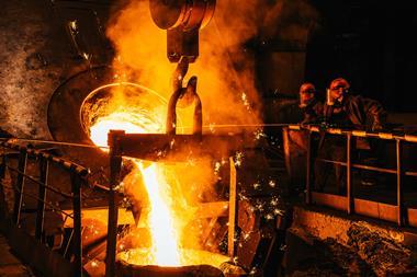 Two workers pouring molten metal from a large crucible into a mould