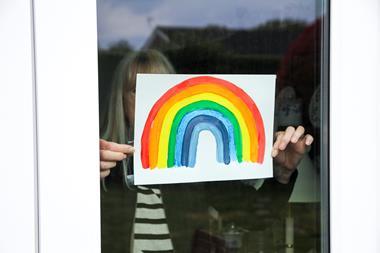 An image showing a woman placing a rainbow drawing on her window